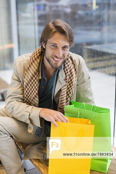 Porträt eines lächelnden Mannes in einer Flughafenlounge mit Einkaufstaschen