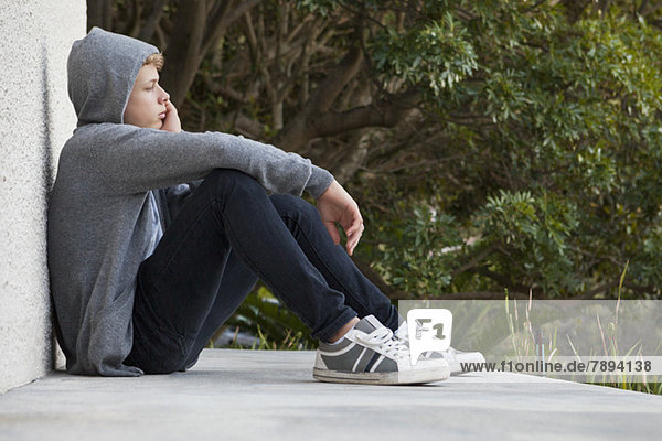 Teenage boy leaning against a wall and thinking
