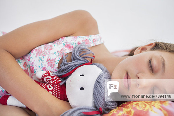 Mädchen schlafend auf dem Bett mit einer Stoffpuppe