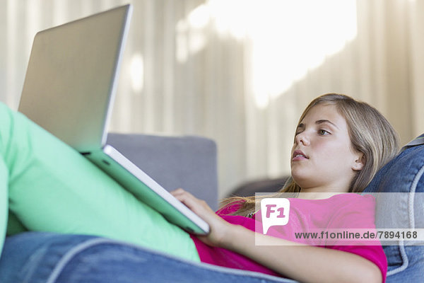 Mädchen,  das auf einer Bohnentüte liegt und einen Laptop benutzt