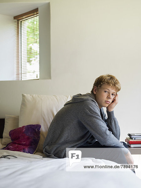 Teenager-Junge sitzt auf dem Bett und denkt nach.