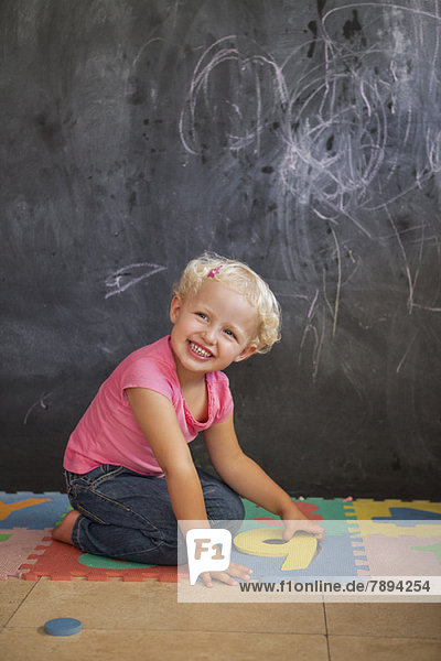 Lächelndes Mädchen spielt mit Zahlenpuzzle vor einer Tafel