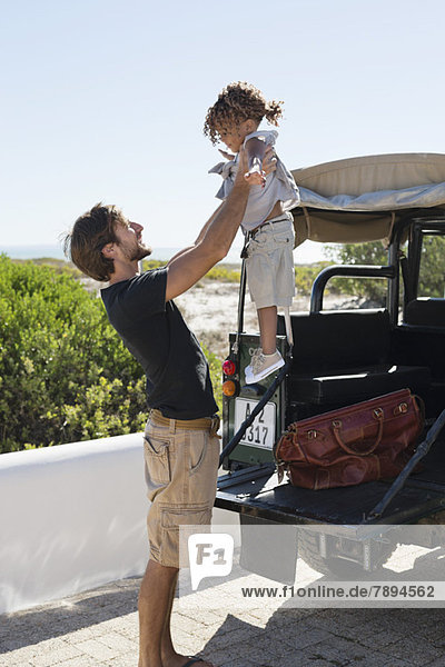 Man playing with his daughter beside a SUV