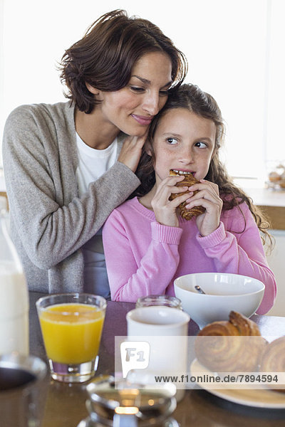 Girl having breakfast beside her mother at a kitchen counter