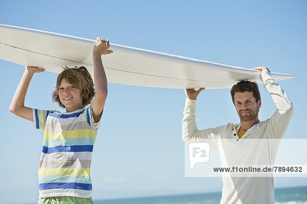 Man and his son carrying a surfboard on the beach
