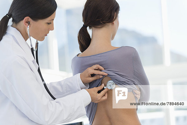 Eine Ärztin untersucht den Rücken einer Frau mit einem Stethoskop.