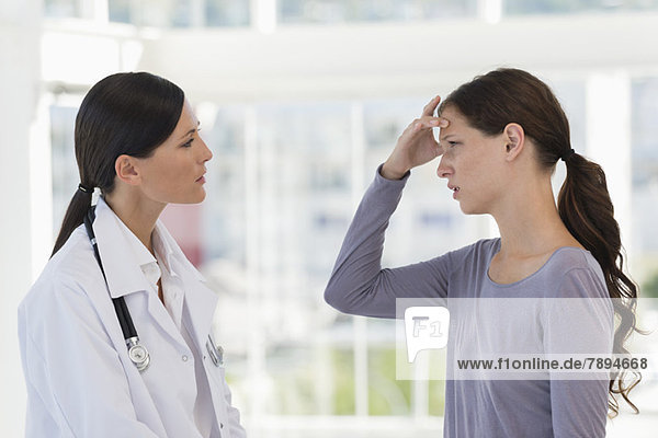 Female patient gesturing headache while discussing with a doctor