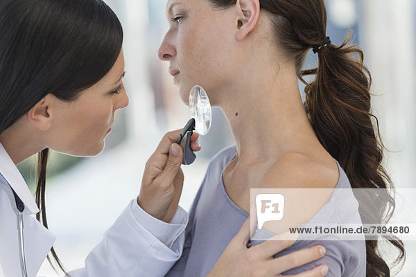 Dermatologe untersucht Frauenhaut mit Lupe