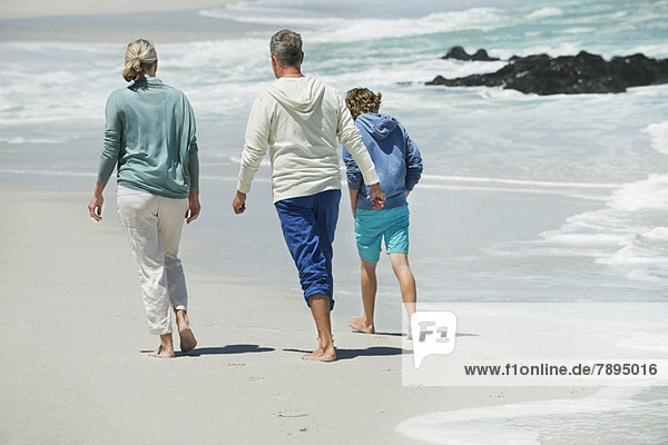 Junge  der mit seinen Großeltern am Strand spazieren geht.