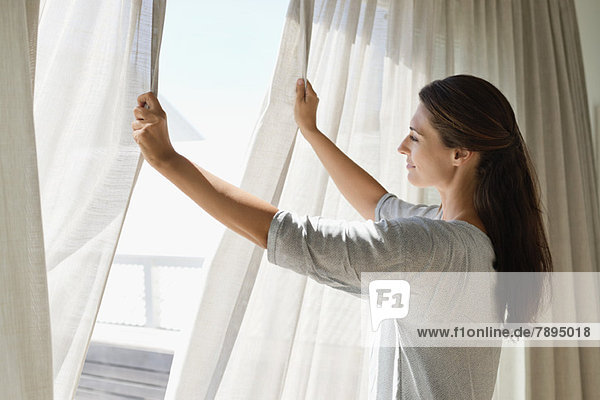Frau öffnet den Vorhang eines Fensters