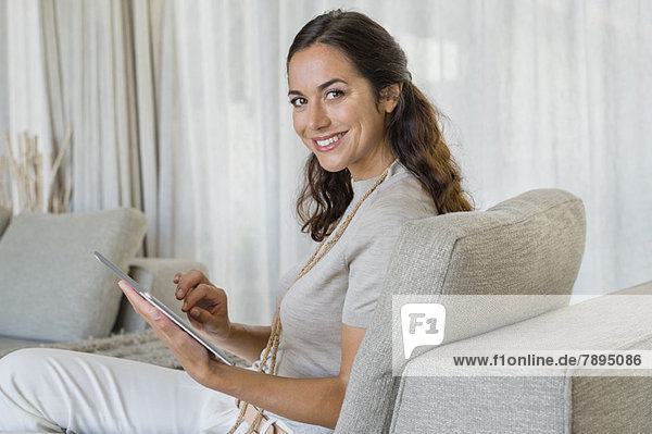 Beautiful woman using a digital tablet and smiling on a couch
