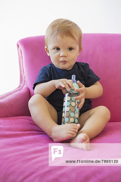 Porträt eines kleinen Jungen  der mit einer Babyflasche sitzt