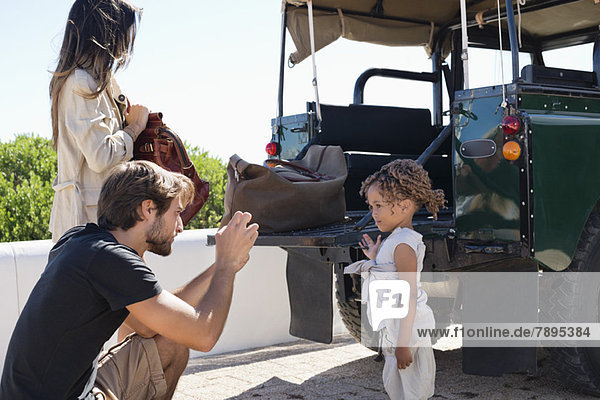 Man taking a picture of his daughter with a smartphone beside a SUV