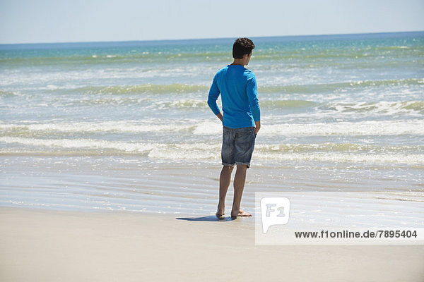 Mann steht am Strand und schaut auf das Meer.