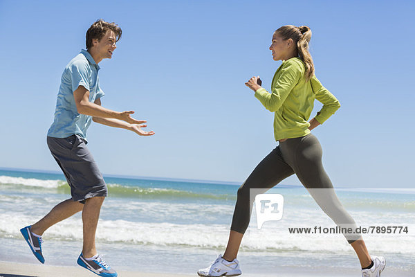 Frau beim Joggen am Strand mit ihrem Trainer