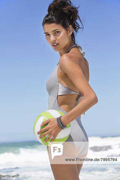 Schöne Frau hält einen Volleyball am Strand.