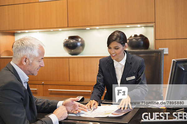 Receptionist showing a brochure to a businessman at a hotel reception counter