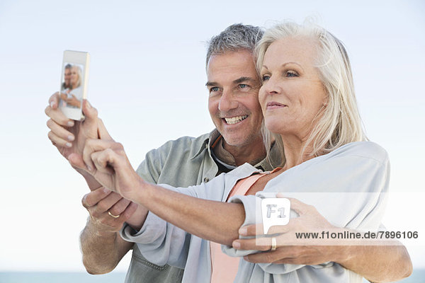Ein Paar macht ein Foto von sich mit einem Handy am Strand.