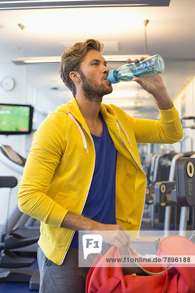 Mann trinkt Wasser aus einer Flasche im Fitnessstudio
