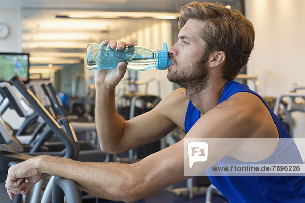 Mann trinkt Wasser aus einer Flasche im Fitnessstudio