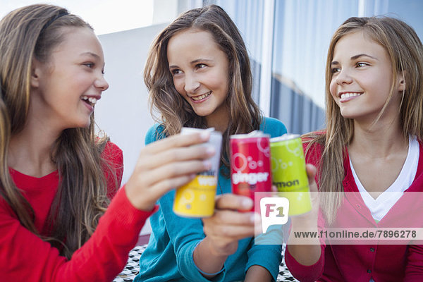 Close-up of three girls toasting with soft drink cans