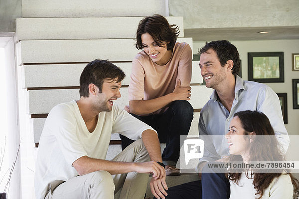 Lächelnde Freunde  die auf Stufen sitzen und miteinander reden.