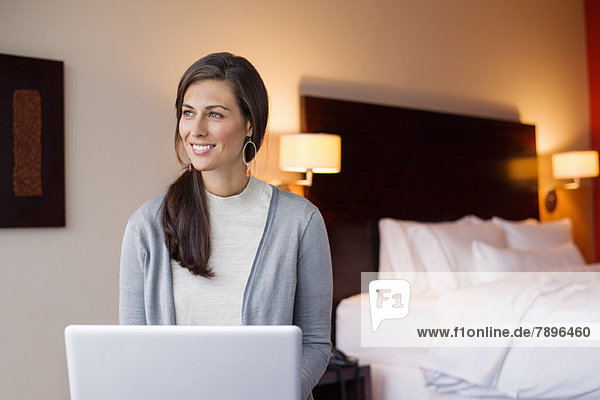 Frau benutzt einen Laptop in einem Hotelzimmer und lächelt
