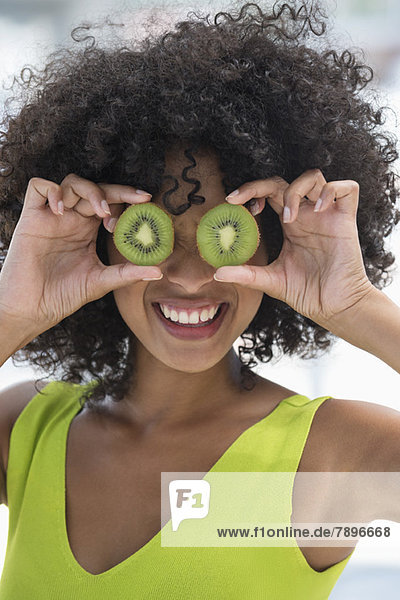Frau hält Kiwifrüchte vor ihren Augen