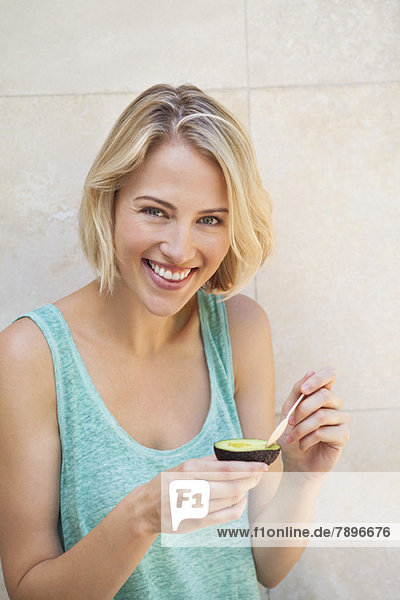 Porträt einer lächelnden Frau beim Essen von Avocado