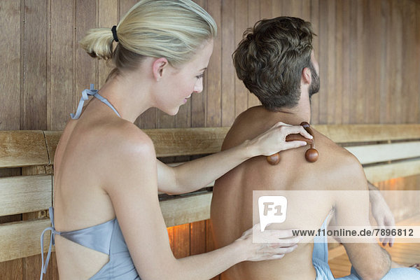 Frau massiert den Rücken ihrer Freundin mit einem Massagegerät in der Sauna.