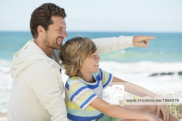 Mann  der mit seinem Sohn auf den Strand zeigt