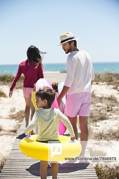 Kinder mit ihren Eltern halten aufblasbare Ringe an einer Strandpromenade.