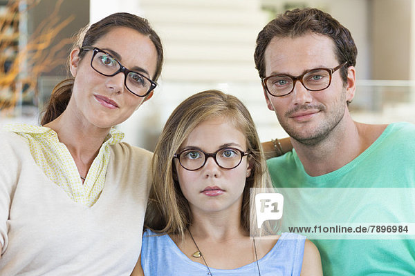 Porträt einer Familie  die auf einer Couch sitzt und eine Brille trägt.