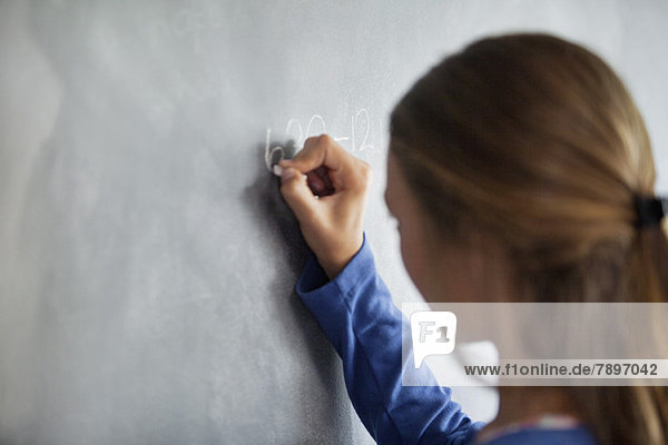 Close-up of a girl writing on a blackboard in a classroom