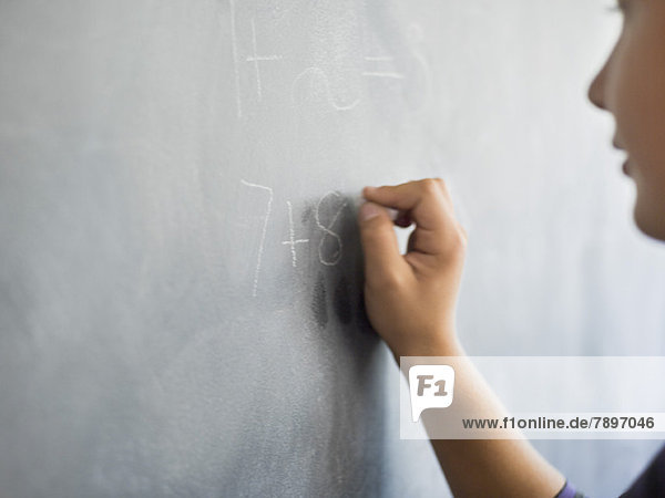 Close-up of a boy writing on a blackboard in a classroom