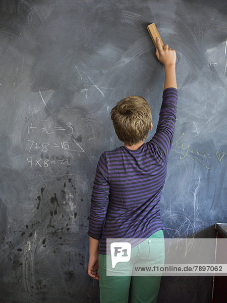 Junge putzt Tafel mit einem Staubwedel im Klassenzimmer