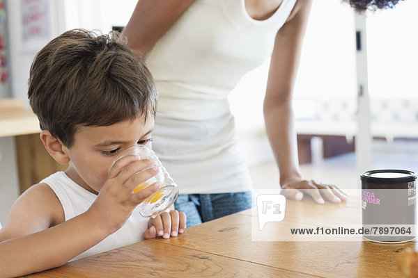 Junge trinkt Orangensaft  seine Mutter steht hinter ihm.