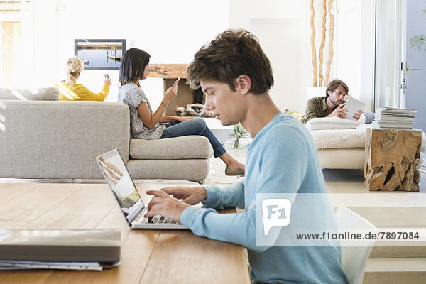 Mann mit einem Laptop und seinen Freunden mit elektronischen Gadgets im Hintergrund