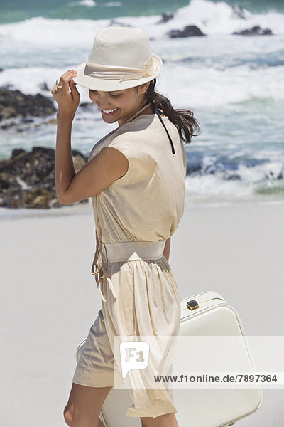 Beautiful woman carrying a suitcase on the beach