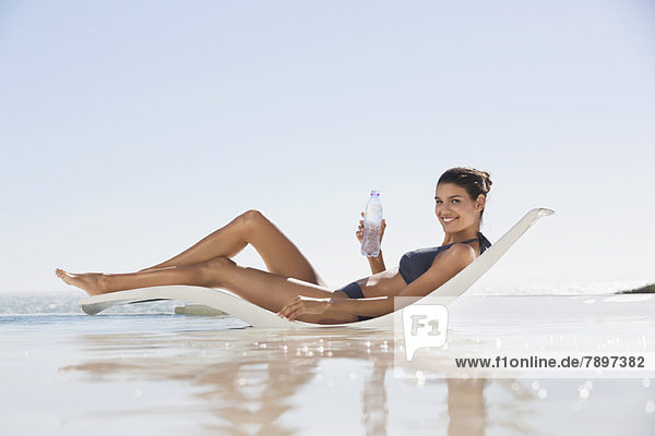 Schöne Frau mit einer Wasserflasche beim Sonnenbaden am Strand