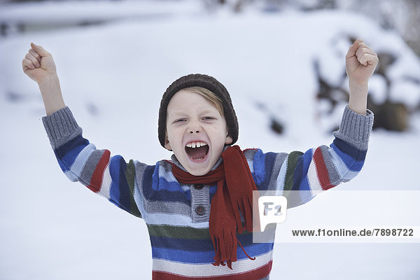 Junge im Winterpullover und Schal  schreit mit erhobenen Fäusten