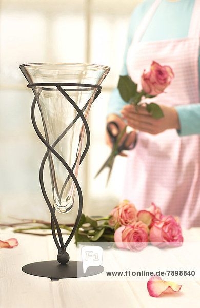 Frau mit Schürze schneidet Rosen für eine Blumenvase