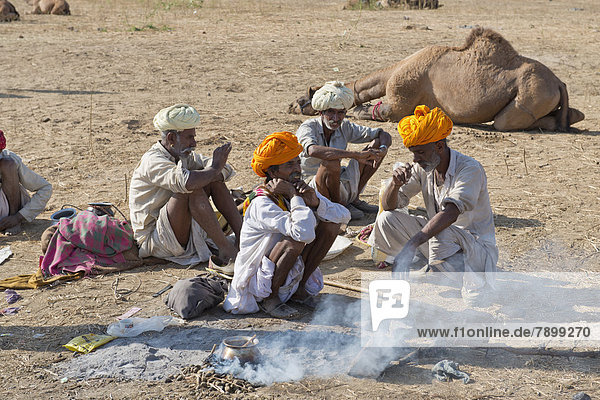 Four elderly Indian men with turbans and wearing the traditional Dhoti garment squatting on the ground  food is being prepared over an open fire  Pushkar Camel Fair