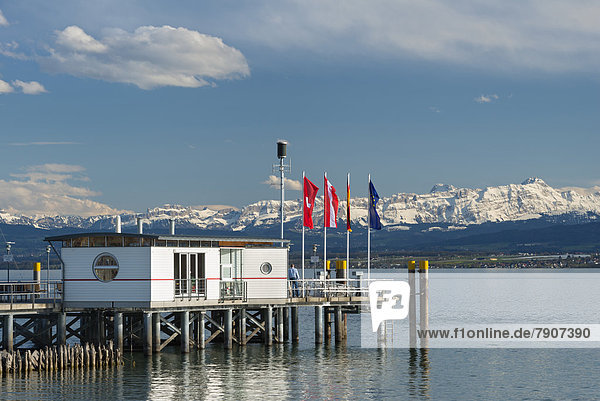 Germany Ferry jetty with flags and snow covered Swiss Alps at Lake Constance