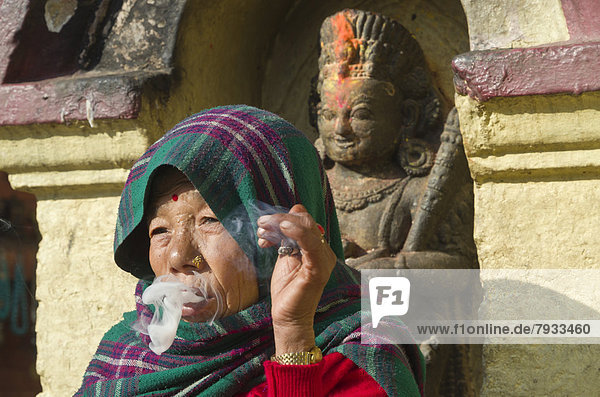 Alte Frau beim Rauchen vor einer Statue