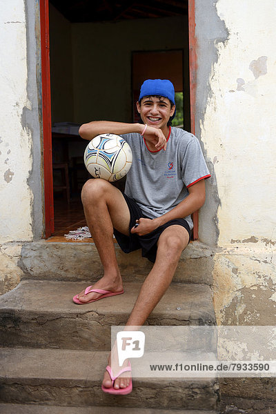 Teenager with football sitting in front of his home in a favela