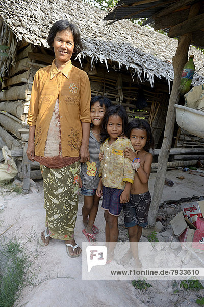 Woman standing with three girls in front of a hut made of wood and straw
