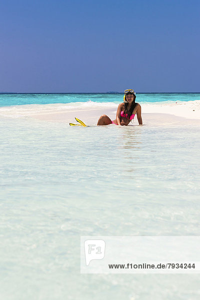 Young woman  about 20  sitting on a sandbank with snorkeling gear