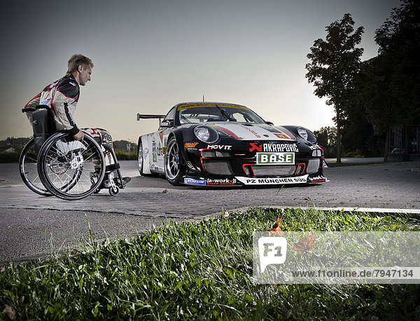 Race car driver in a wheelchair  next to his Porsche race car