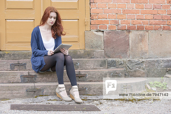 Young woman sitting on stairs in front of building holding a tablet pc